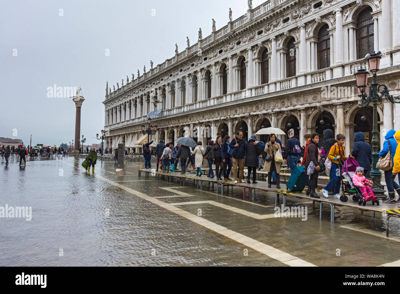 Les gens qui marchent sur les plates-formes élevées au cours d'une acqua alta (haute) de l'eau de cause à la Biblioteca building, Piazzetta di San Marco, Venise, Italie Banque D'Images