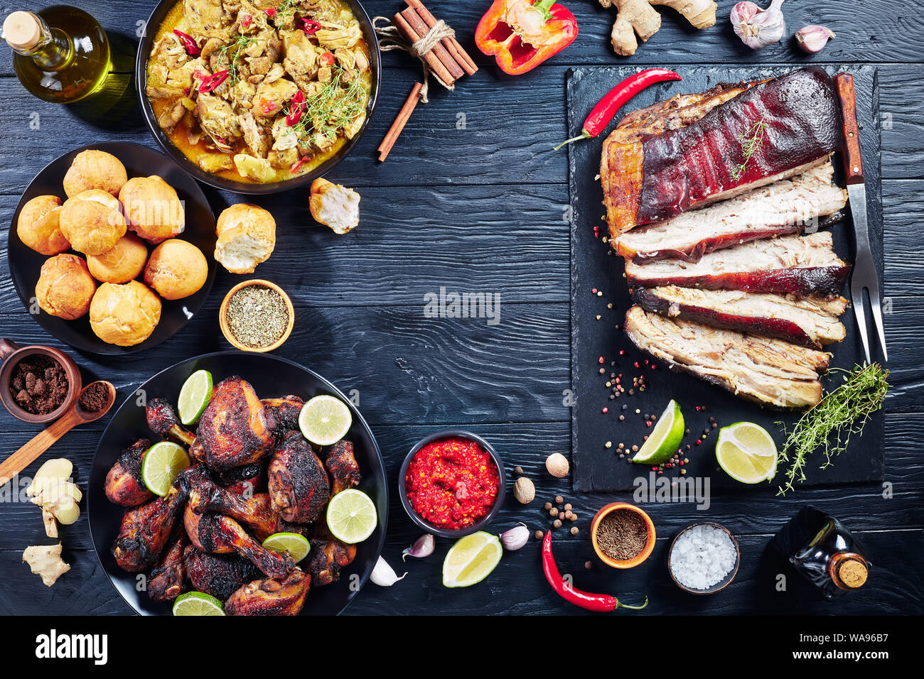 Ensemble de plats des caraïbes, porc, Jerk Chicken curry, poêlée de cuisses de poulet rôti, quenelles et baguettes sur les plaques sur une table en bois noir, vie Banque D'Images