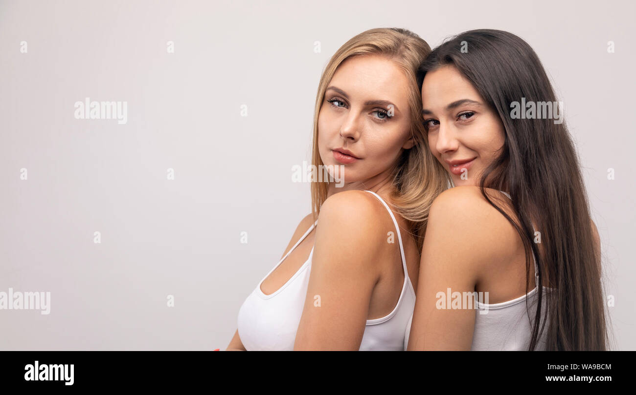 Jeune blonde et brune en camisoles blanches niché les uns les autres à la caméra à l'arrière-plan blanc isolé copyspace Banque D'Images