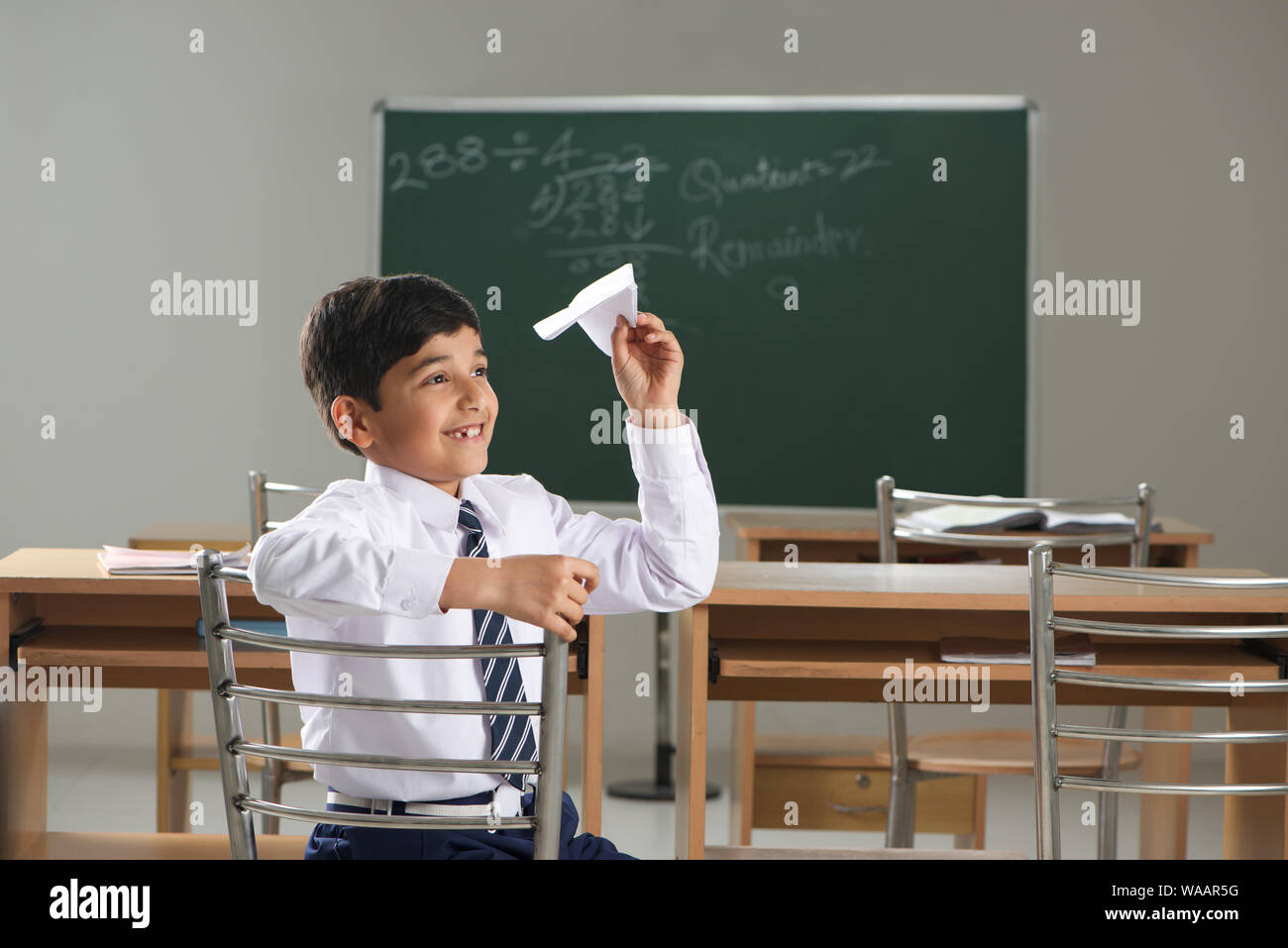 Un écolier jouant avec un avion en papier dans une salle de classe Banque D'Images