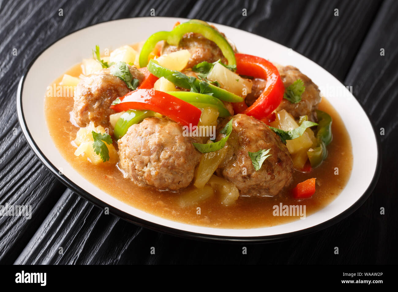 Boulettes asiatiques à l'étuvée avec ananas frais et poivrons dans une sauce aigre-douce close-up sur une plaque sur la table horizontale. Banque D'Images