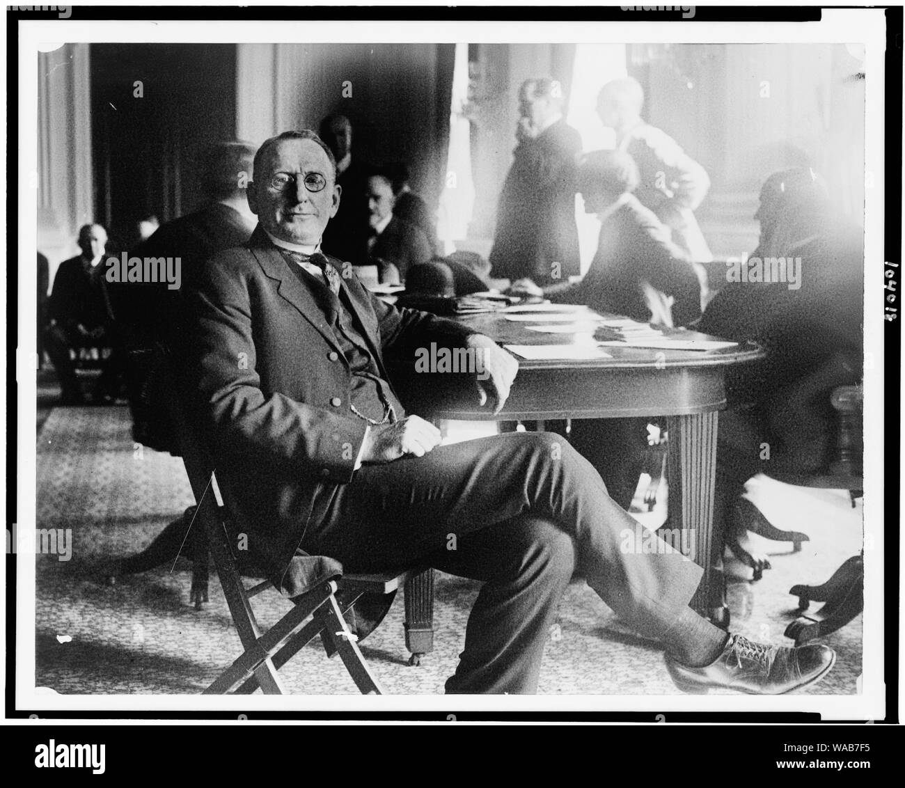 Le colonel William Joseph Simmons, portrait en pied, assis à table au cours de la Chambre chargé d'enquête sur le Ku Klux Klan ; hommes debout et assis en arrière-plan Banque D'Images