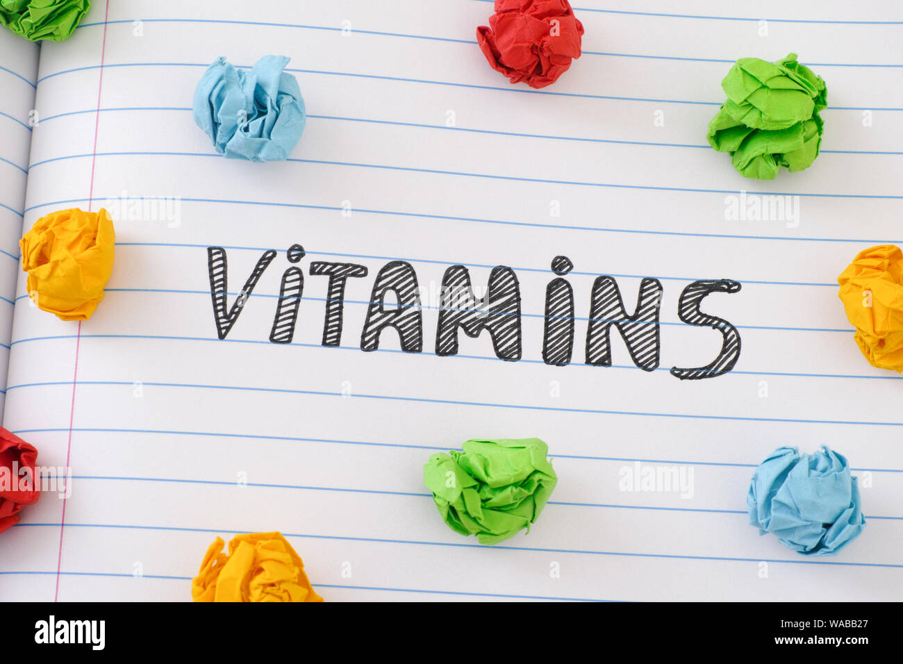 Le mot Vitamines sur feuille portable avec quelques boules de papier froissé colorés autour de lui. Close up. Banque D'Images