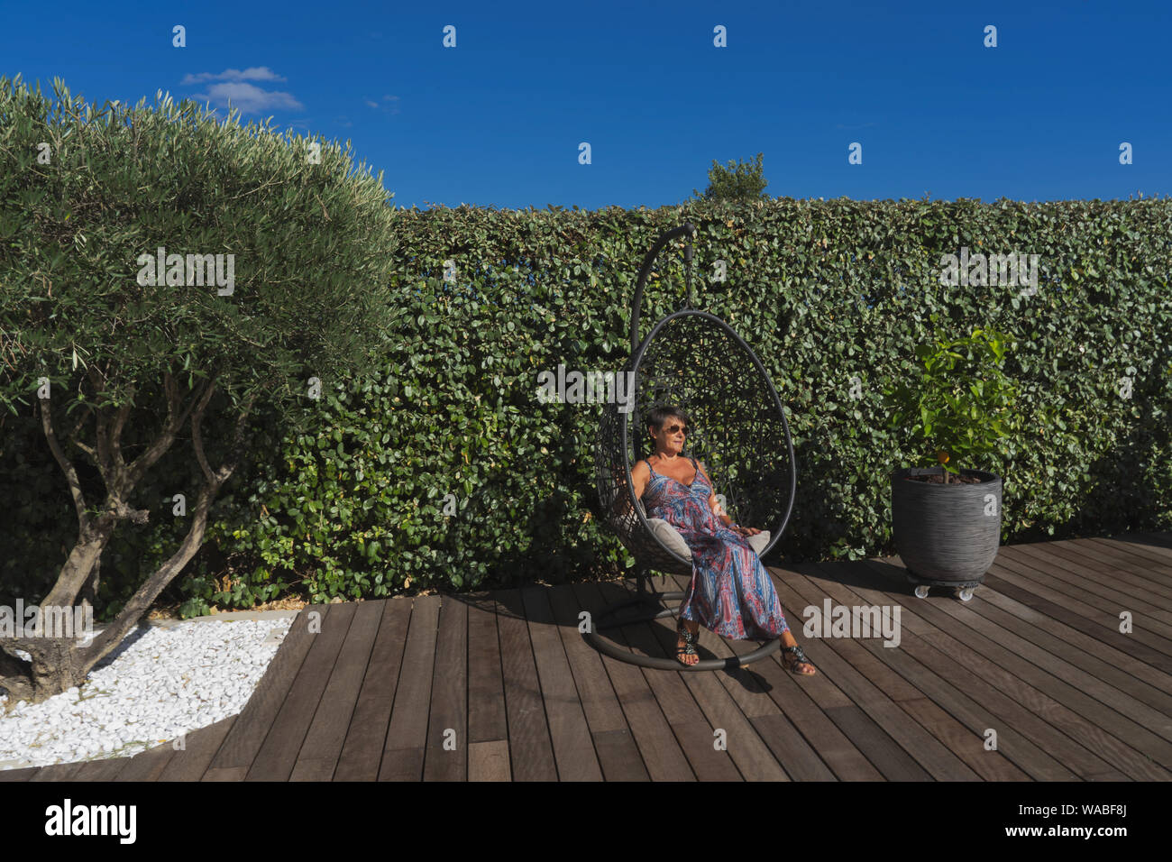 Une femme s'asseoir dans un siège suspendu sur un sol en bois dans un jardin avec un olivier Banque D'Images