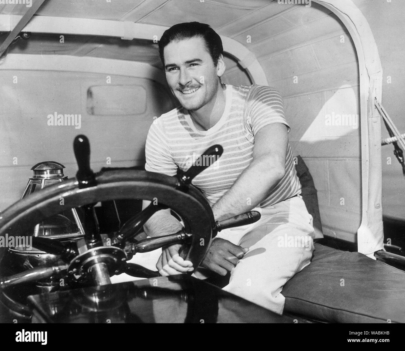 Errol Flynn, vêtu d'une chemise rayée et sourire comme il est assis avec les mains sur le volant d'un commandant de yacht, circa (1945) #  de dossier 33848-463THA Banque D'Images