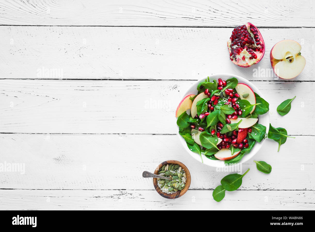 Des épinards, salade de pomme de grenade sur fond de bois blanc, copie de l'espace. Végétalien sain salade d'automne et d'ingrédients. Banque D'Images