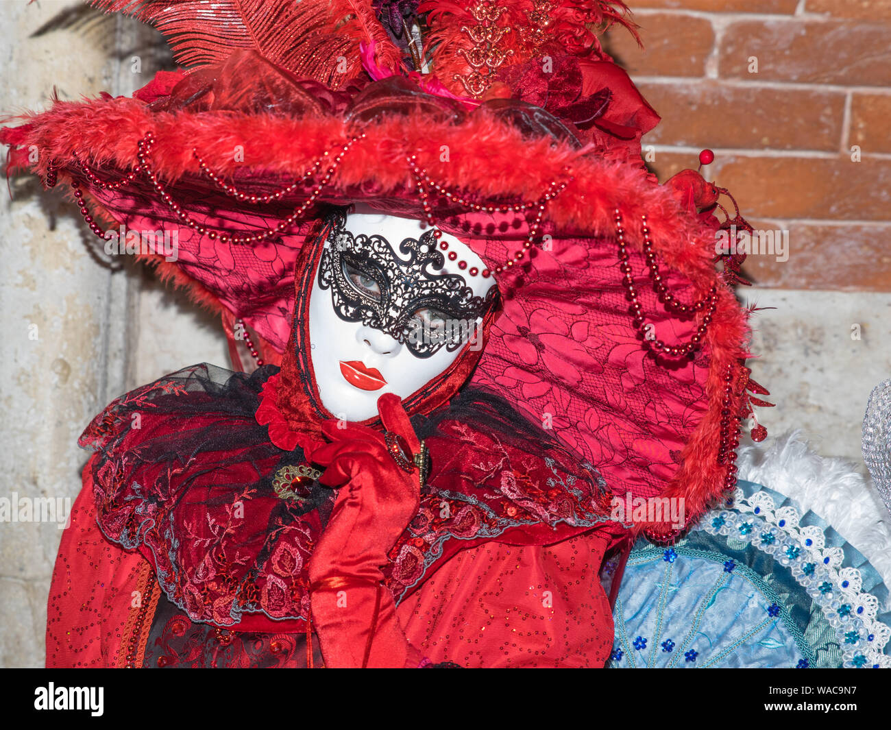 Dame en costume rouge et blanc masque au carnaval de Venise. Très décoratif brillant costume avec détails, yeux visible derrière le masque. Old wall background Banque D'Images