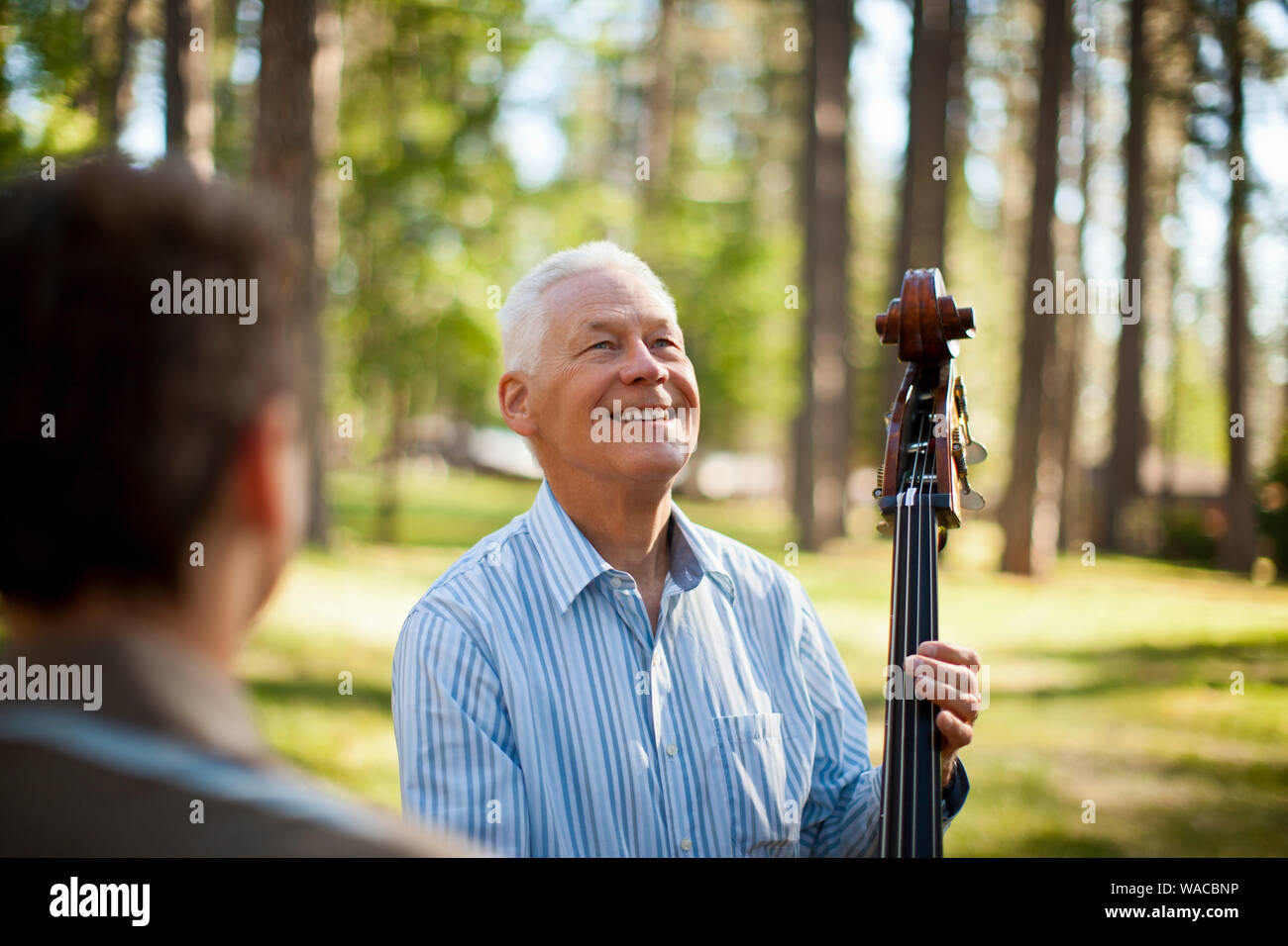Smiling senior man holding le cou d'une contrebasse dans une forêt. Banque D'Images