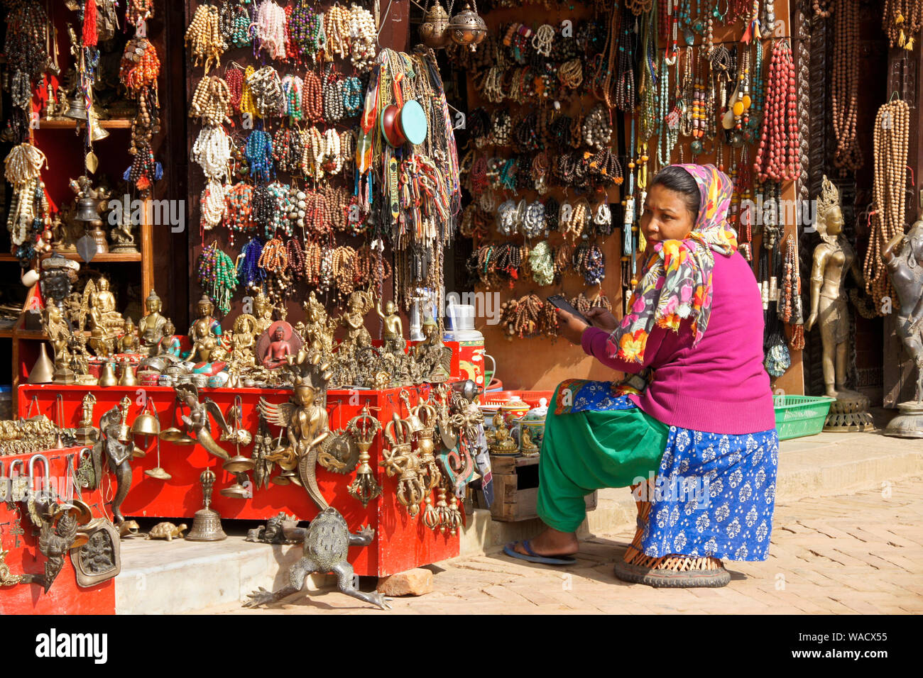 Femme assise en face de magasin qui vend des perles de prière bouddhiste tibétain et d'autres objets religieux à Boudhanath, Vallée de Katmandou, Népal Banque D'Images
