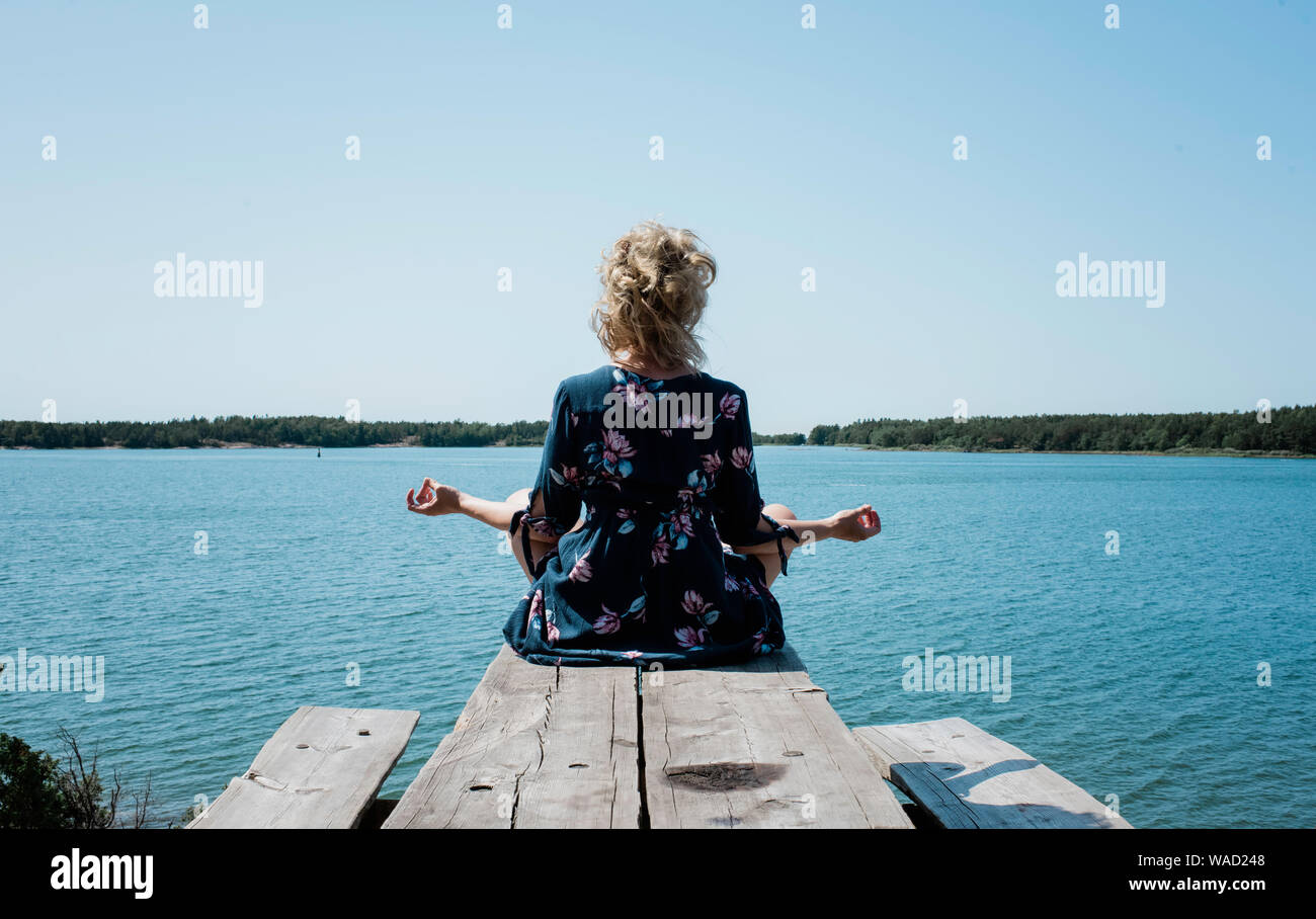 Femme méditant assis à l'extérieur face à la mer en vacances Banque D'Images