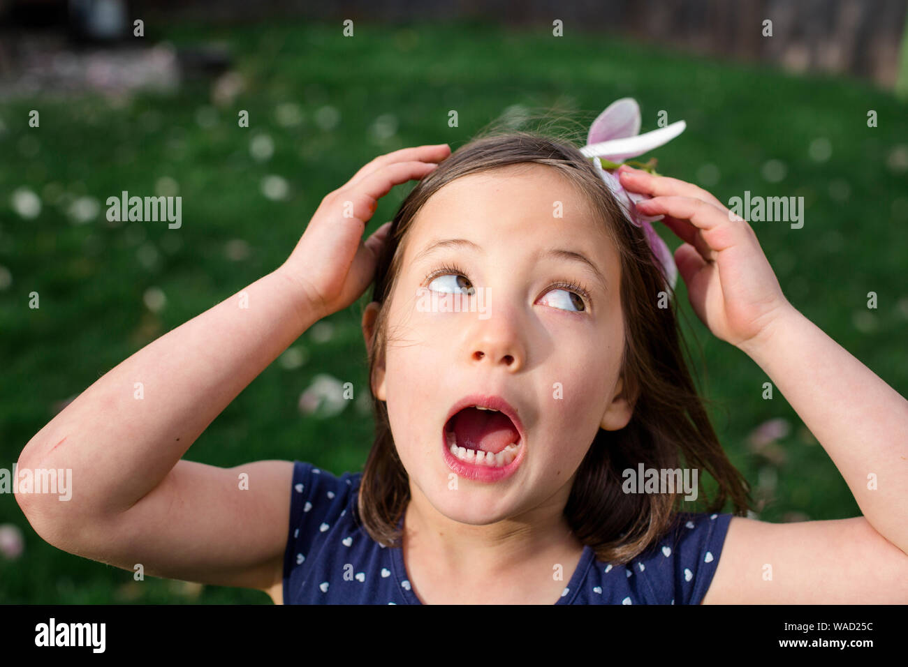 Une petite fille sur une breezy day détient une fleur fleur sur la tête comme un chapeau Banque D'Images