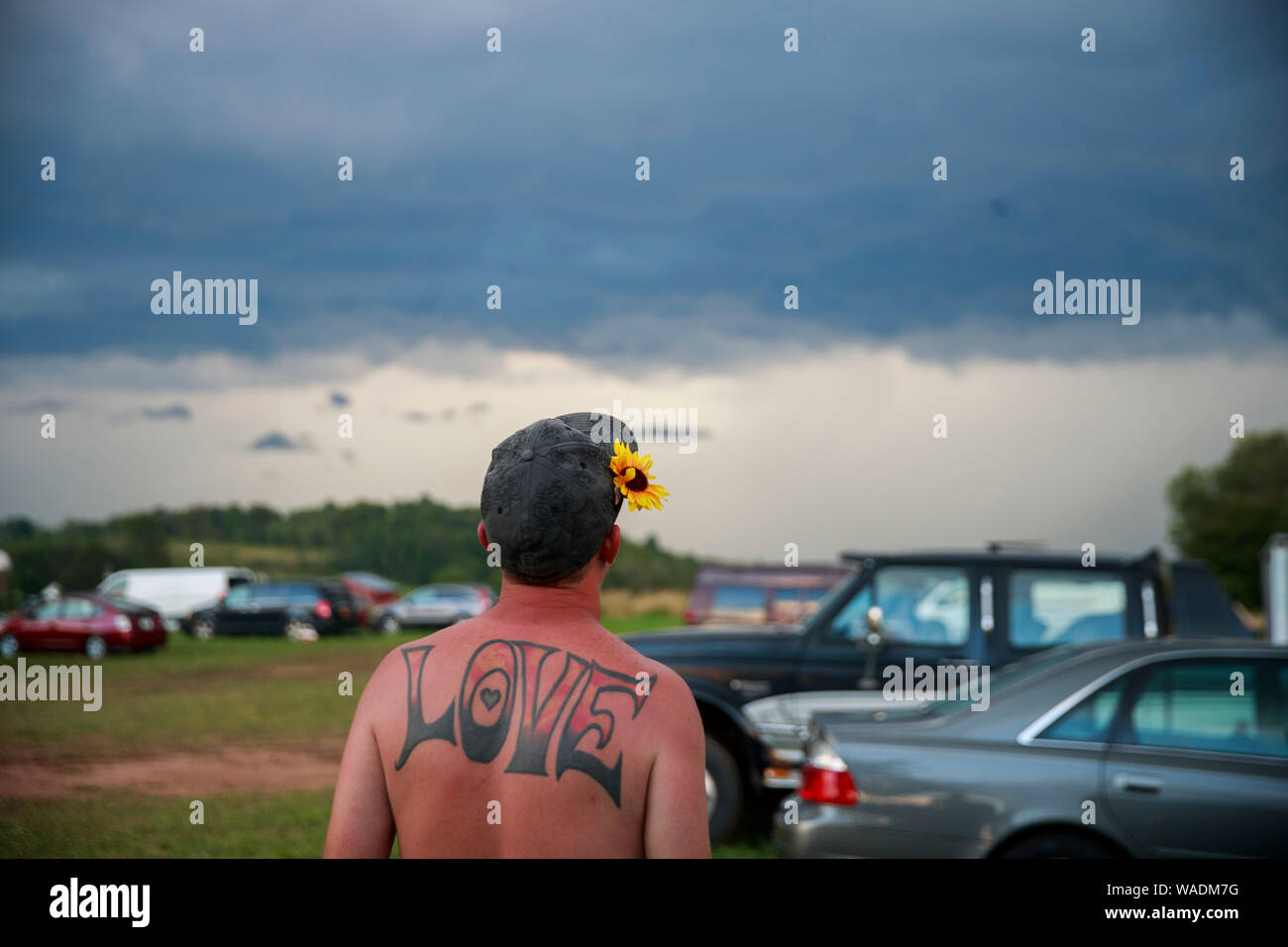 Béthel, United States. Août 18, 2019. Un homme avec un tatouage de l'orthographe, 'Amour', et une fleur dans ses cheveux ressemble à un orage sévère venant en sens inverse sur la dernière journée au cours de la réunion de la route Yasgur Max Yasgur's farm à pendant les célébrations du 50e anniversaire de Woodstock près de Bethel. Organisateur de Woodstock Michael Lang, l'événement a été annulé mais anniversaire les activités ont continué au Arrowhead Ranch, Bethel Woods (le site de l'original Woodstock en 1969), Hector's Inn, et Yasgur's Farm. Credit : SOPA/Alamy Images Limited Live News Banque D'Images