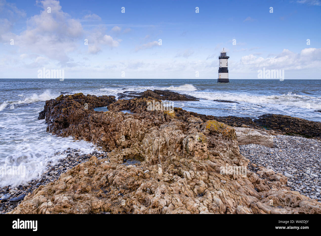 Phare de Penmon Point, Anglesey, au nord du Pays de Galles par un jour de vent avec des vagues se brisant sur l'Estran Banque D'Images