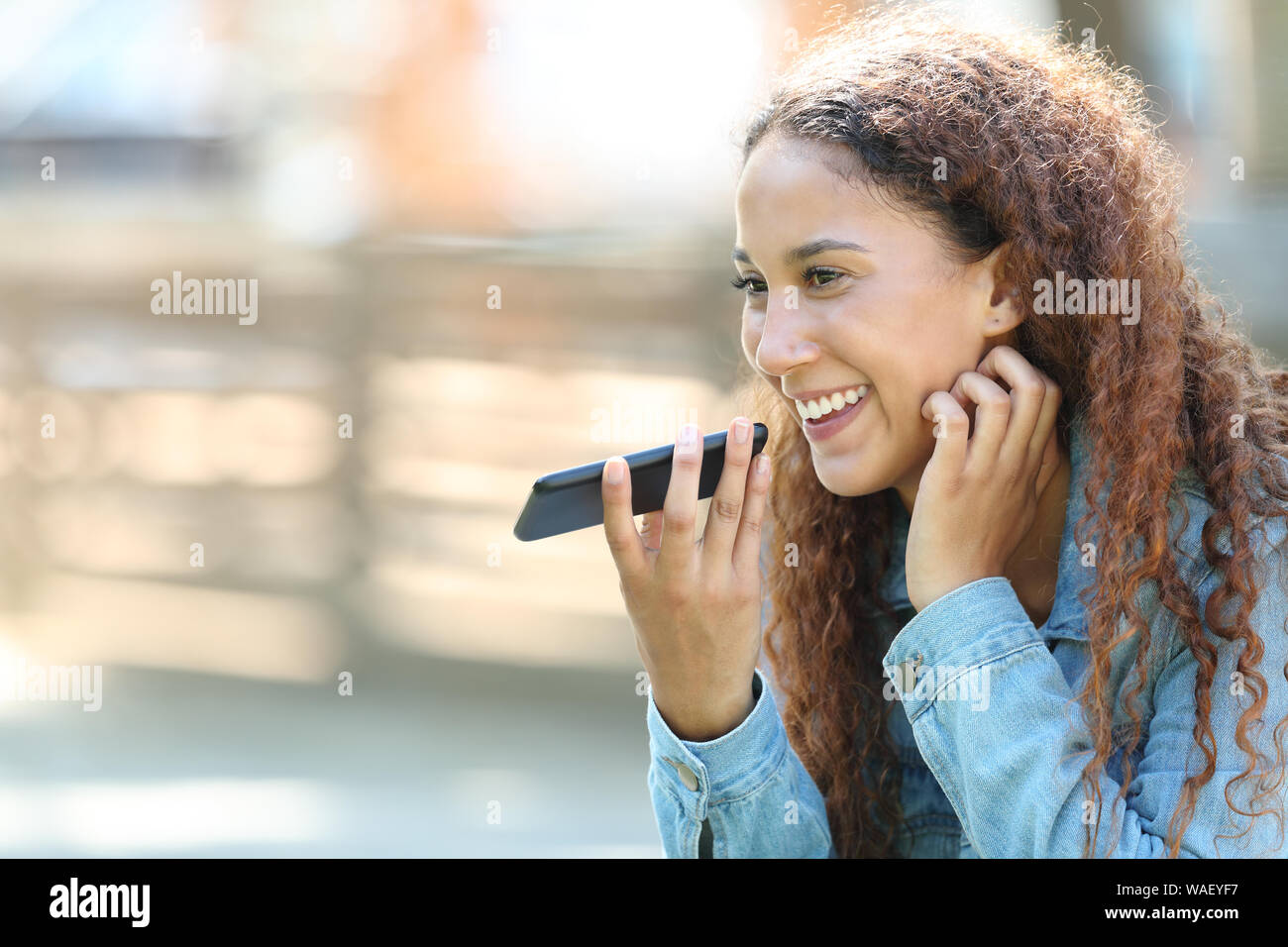 Happy mixed race woman-utilisant la reconnaissance vocale sur téléphone intelligent à l'enregistrement de messages dans un parc Banque D'Images