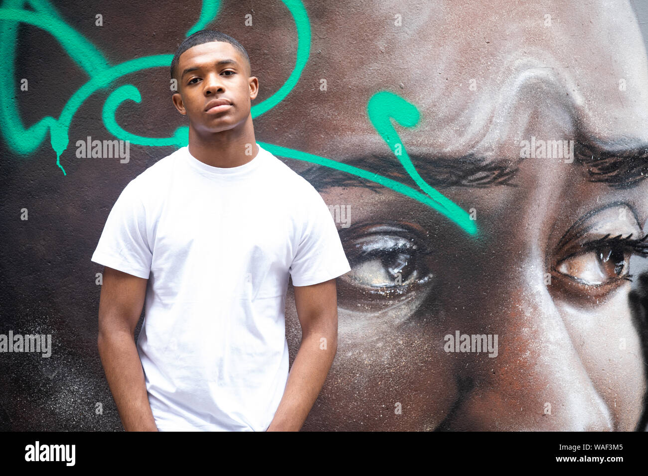 Un jeune homme pose devant un mur de graffiti art portrait sur une rue de ville n London Banque D'Images