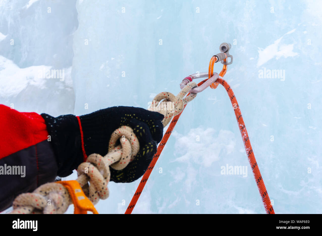 Cascade de glace d'ancrage avec broche à glace, corde de sécurité, mousquetons et bras du grimpeur, gros plan Banque D'Images