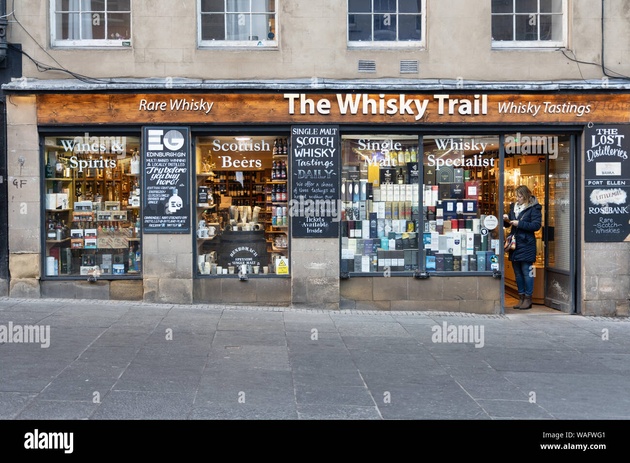 Shop avant du Whisky Trail affichant des bouteilles de whisky avec une dame à l'entrée. High Street, Royal Mile, Edinburgh Scotland UK Banque D'Images
