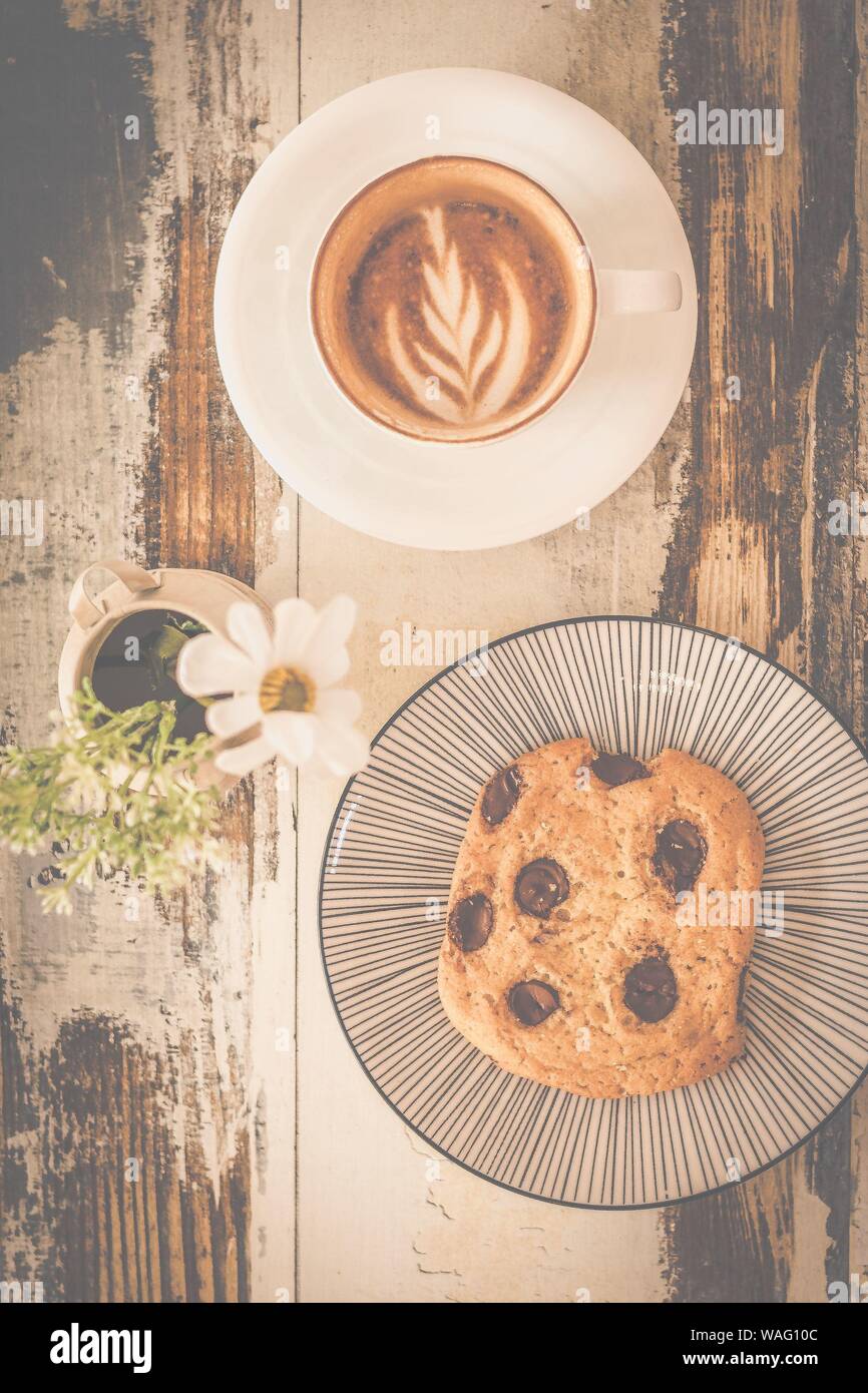 Big chocolate chip cookie avec une tasse de cappunico avec latte art sur le dessus et un petit vase de fleurs Banque D'Images