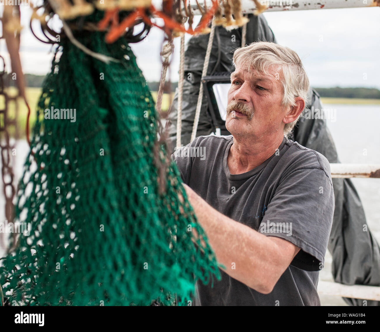 Weathered pêcheur commercial réparant un filet sur un bateau au large de la côte de la Caroline du Sud. Banque D'Images