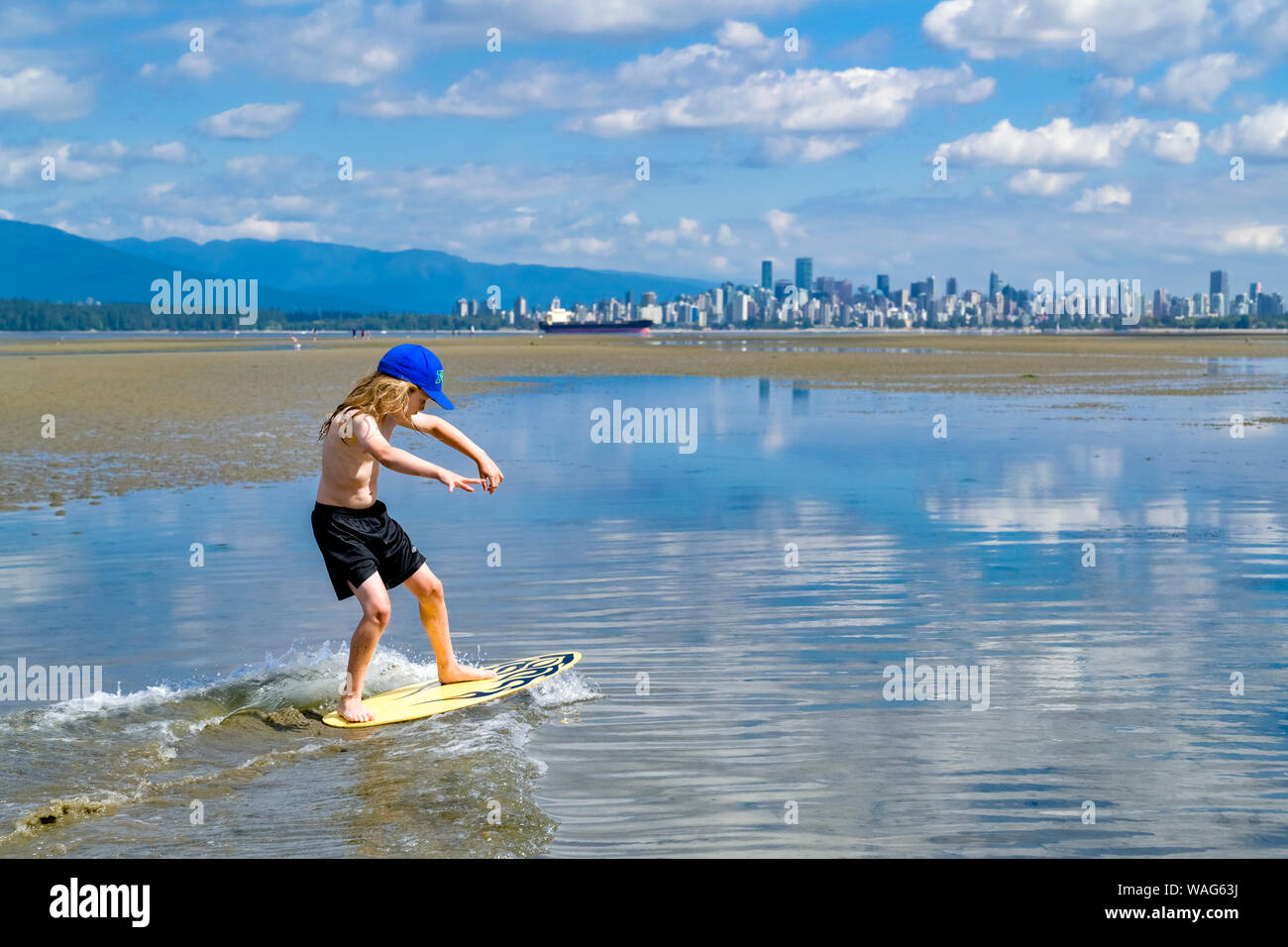 Jeune garçon aux cheveux longs, skimboarding banques espagnoles, English Bay, Vancouver, British Columbia, Canada Banque D'Images
