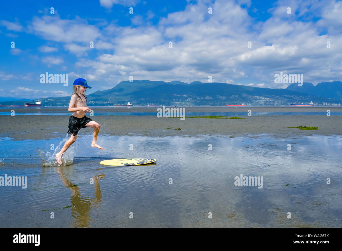 Jeune garçon aux cheveux longs, skimboarding banques espagnoles, English Bay, Vancouver, British Columbia, Canada Banque D'Images