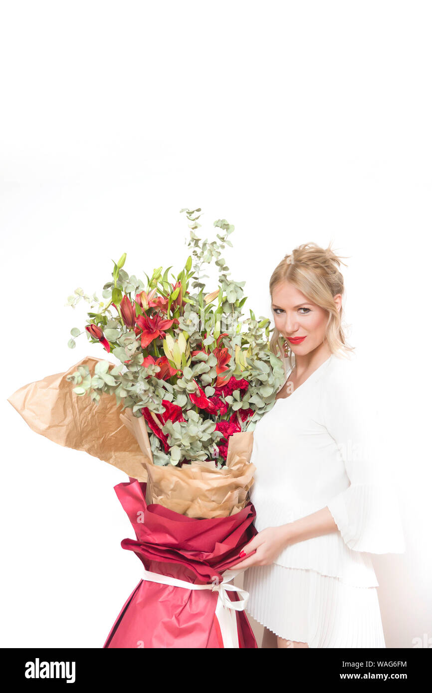 Belle jeune femme blonde holding big bouquet de fleurs colorées contre le mur blanc Banque D'Images