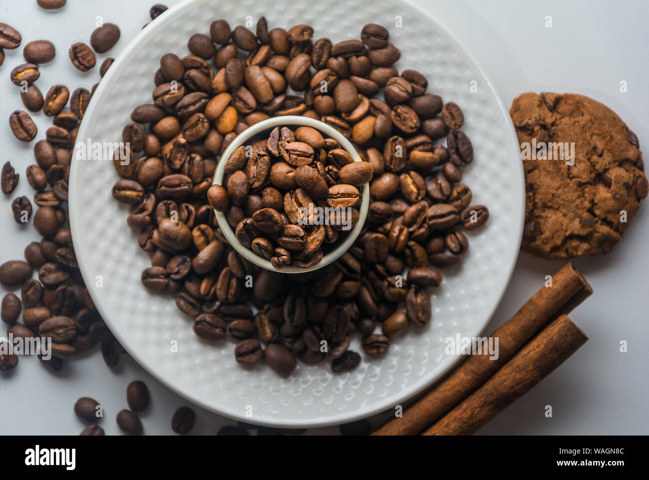 Tasse de café blanc avec grains de café torréfié, de cannelle et de biscuits isolées sur fond blanc à partir de ci-dessus. Les grains de café sur la plaque et dans la tasse. Banque D'Images