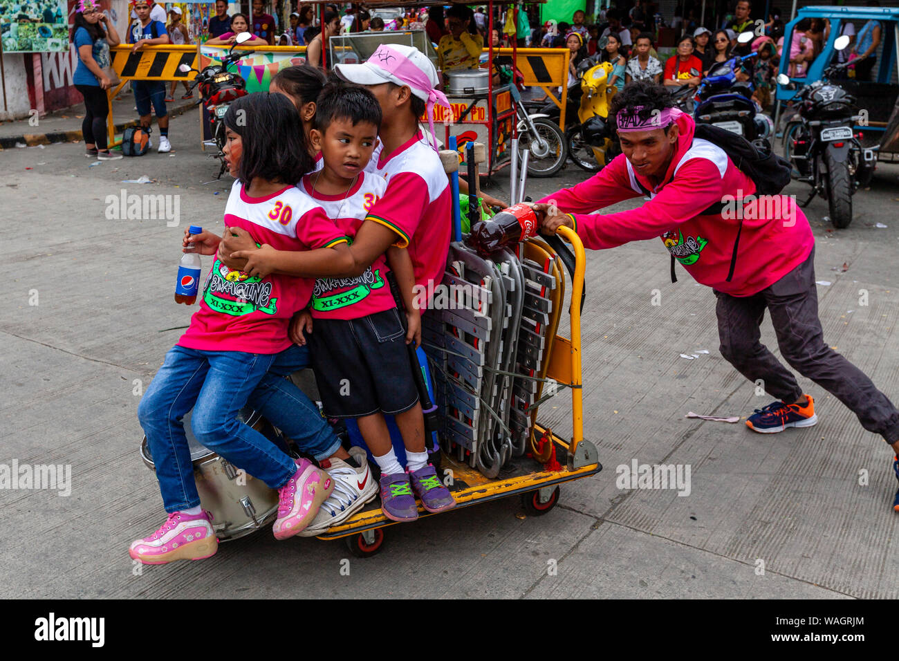 Un jeune homme pousse un groupe d'enfants autour de sur un chariot, l'Ati-Atihan Festival, Pamukkale, l'Île Panay, Province d'Aklan, Philippines. Banque D'Images