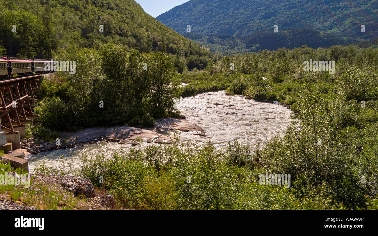 Un train touristique sur la route du col blanc traverse sur une rivière qui traverse une forêt mixte près de Skagway en Alaska Banque D'Images