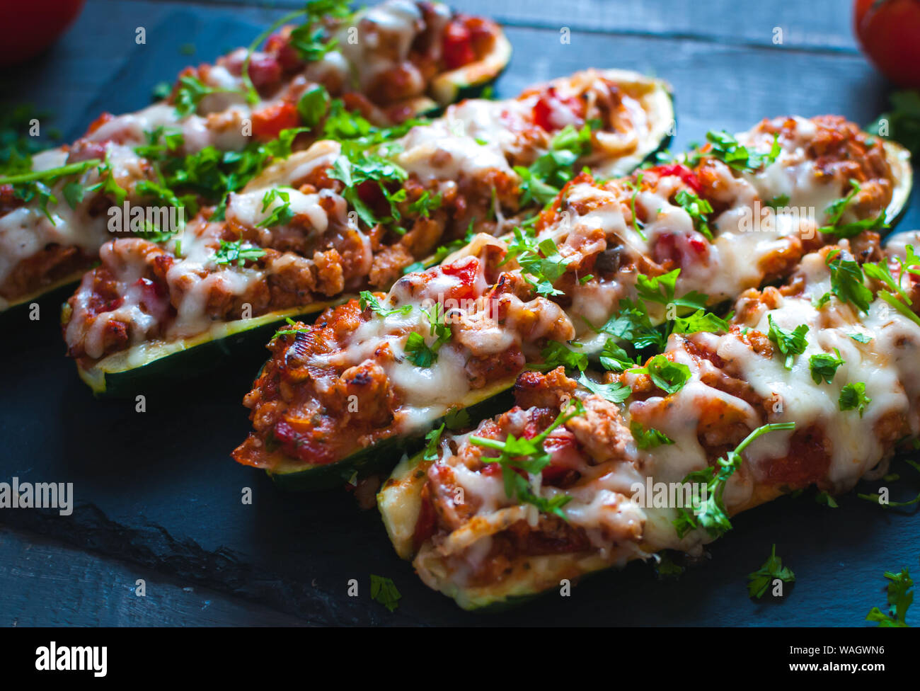 Close-up de bateaux courgettes farcies avec du boeuf haché, sauce tomate, fromage et persil frais, sur fond sombre Banque D'Images