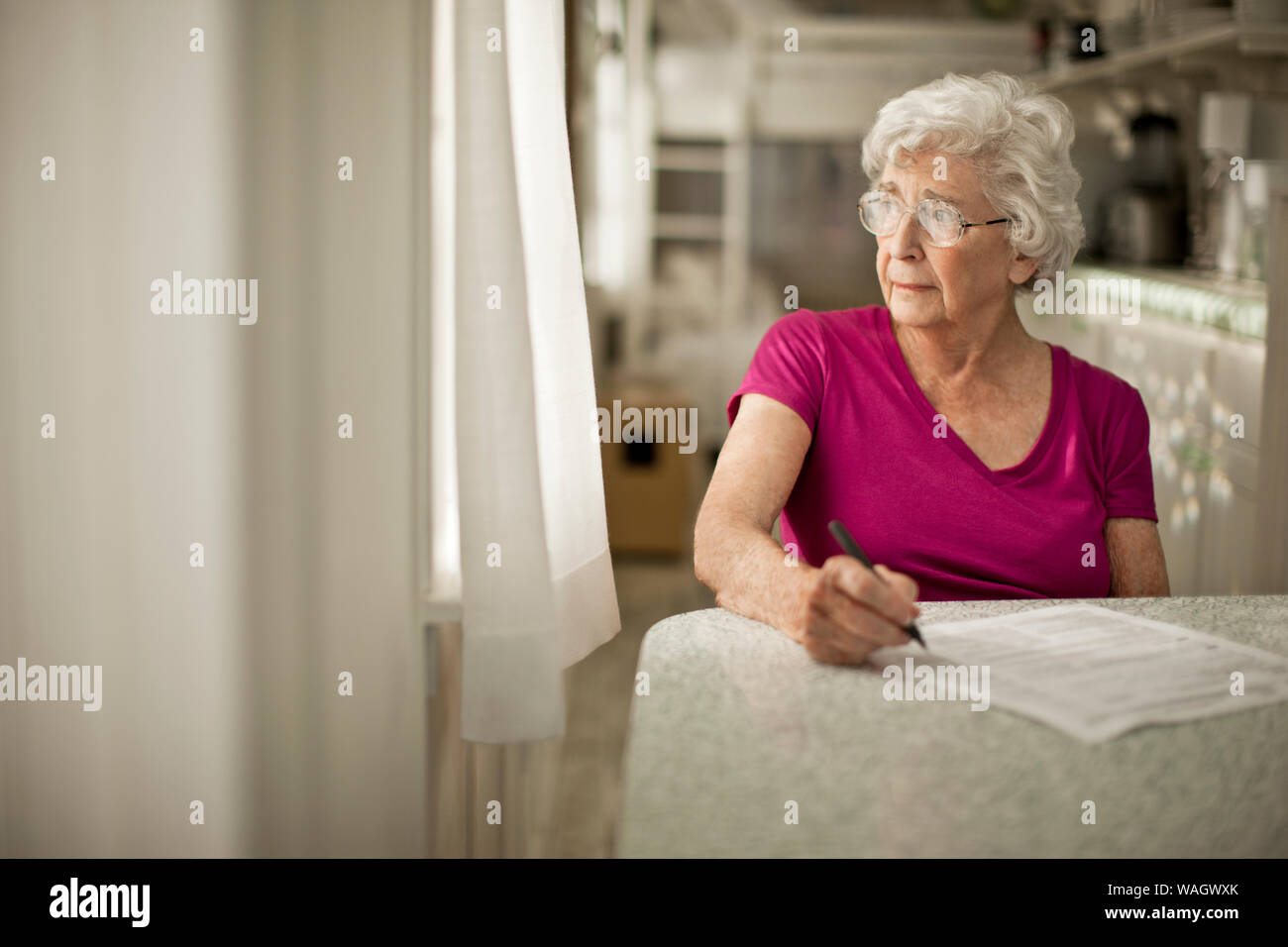 Hâte femme âgée regarde hors de la fenêtre de la cuisine comme elle débats signature quelques formalités administratives. Banque D'Images
