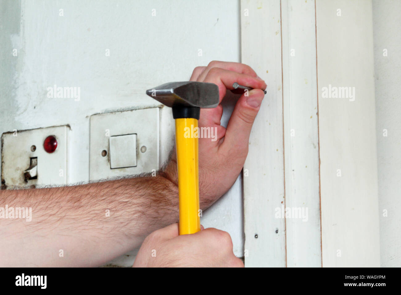 Travailleur de la construction et l'homme à travailler sur des travaux de rénovation. Builder avec marteau frappe jaune et des ongles un clou dans le mur en bois de porte de la cuisine. Banque D'Images