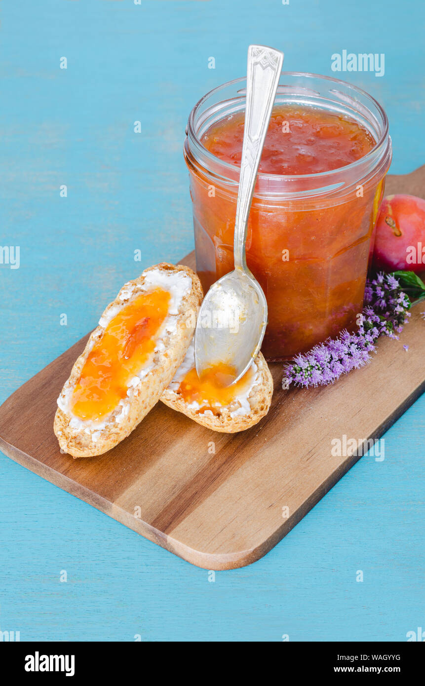 Confiture de prunes maison dans un bocal en verre sur la table de bois et fond bleu. Banque D'Images