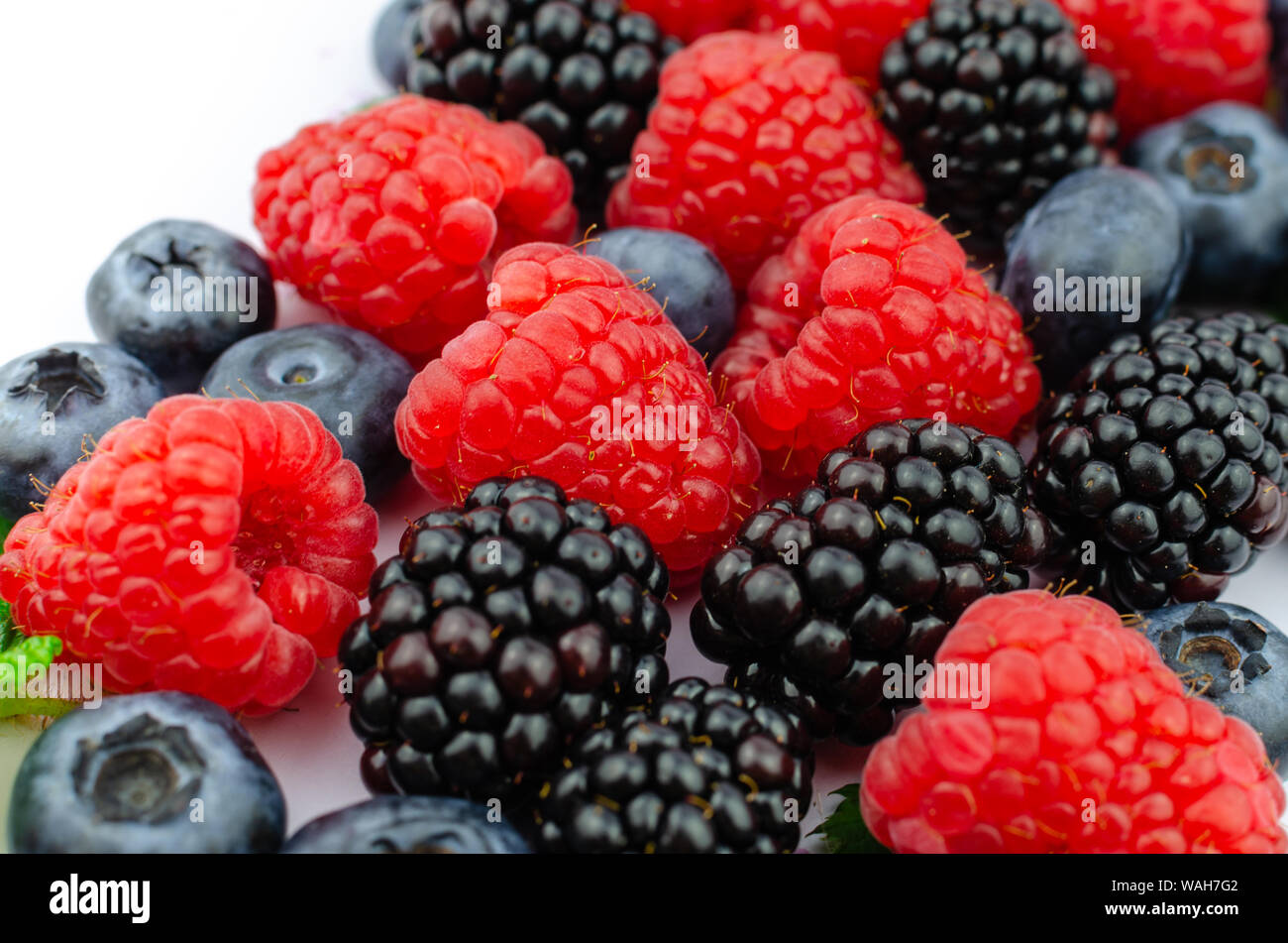 La photo en gros plan de bleuets biologiques, mûres, framboises et feuilles vertes mélangées. Banque D'Images