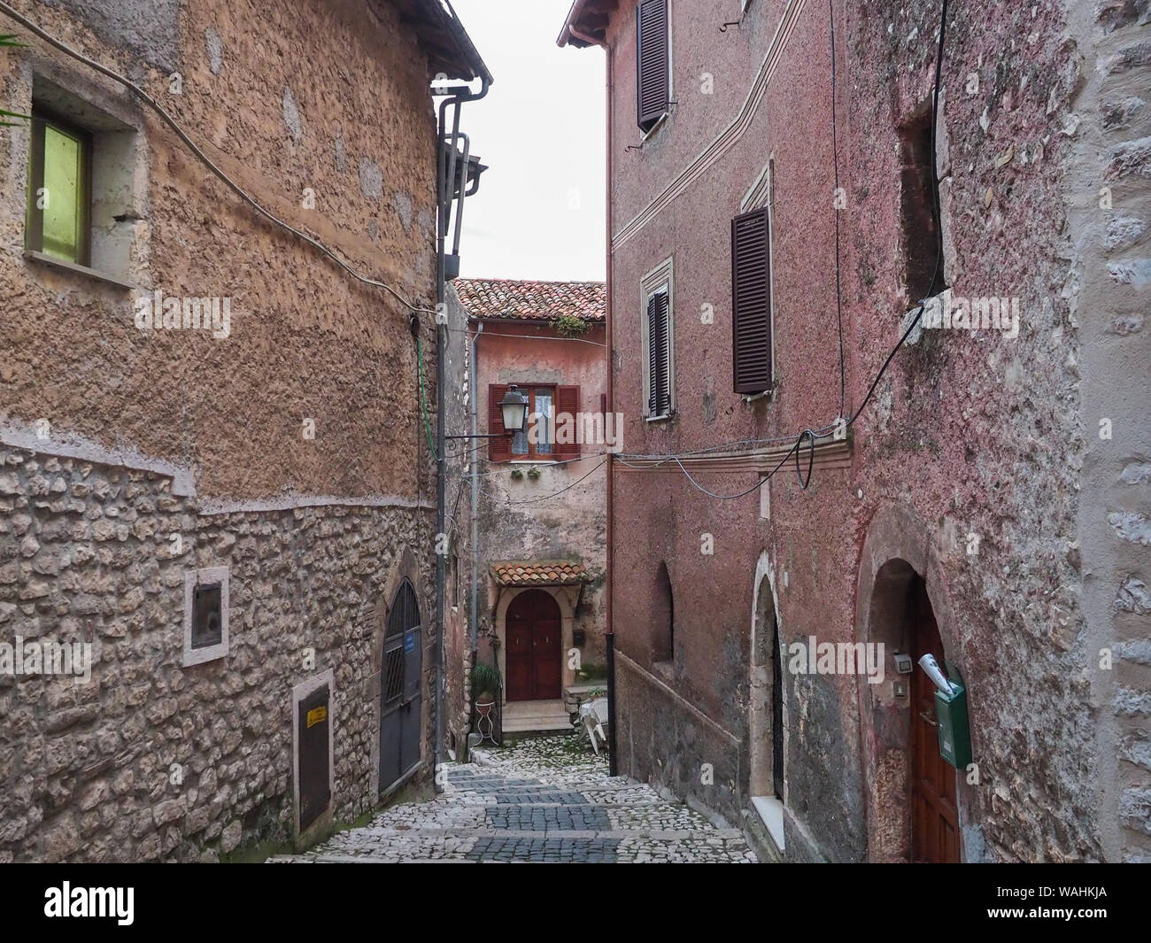 Une étroite rue pavée et maisons médiévales avec portes en bois cintrées rideaux métalliques également sur les fenêtres de petite ville ancienne Sermoneta, Italie Banque D'Images