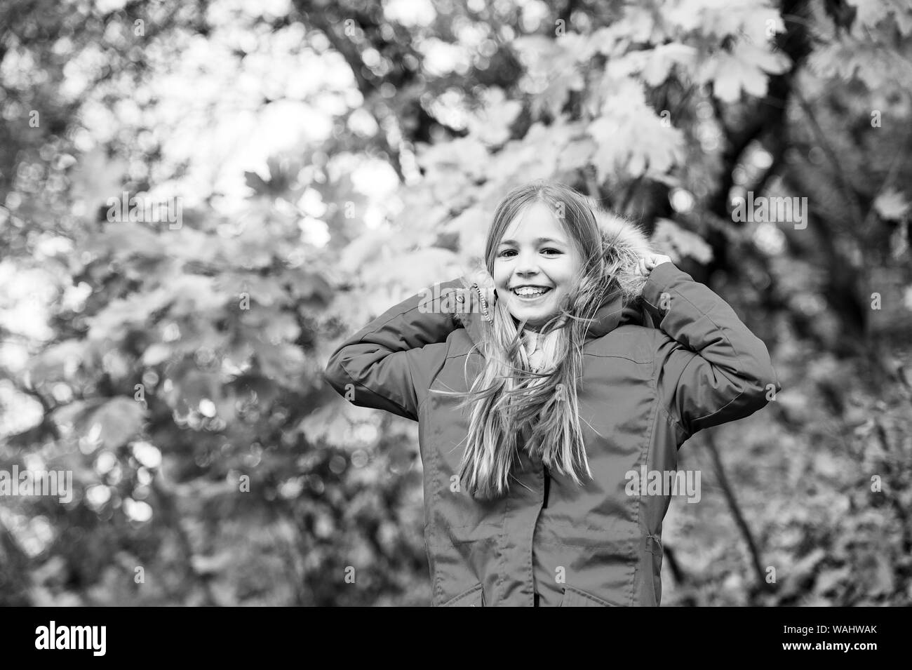 Se sentir confortable en veste chaude. Fille avec capuche manteau usure automne profitez de la nature. Manteau pour porter l'enfant saison d'automne. Vêtements d'automne et de la mode concept. De longs cheveux blonds de l'enfant parc automne marche arrière-plan. Banque D'Images