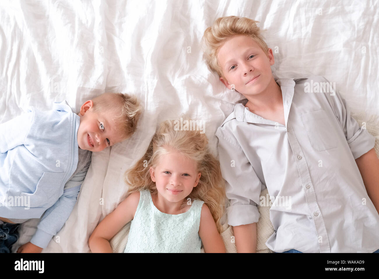 Trois cheerful blonde enfants sont couchés ensemble sur le lit, et sourit. Deux garçons et une fille. Famille heureuse, frères et soeur. Banque D'Images