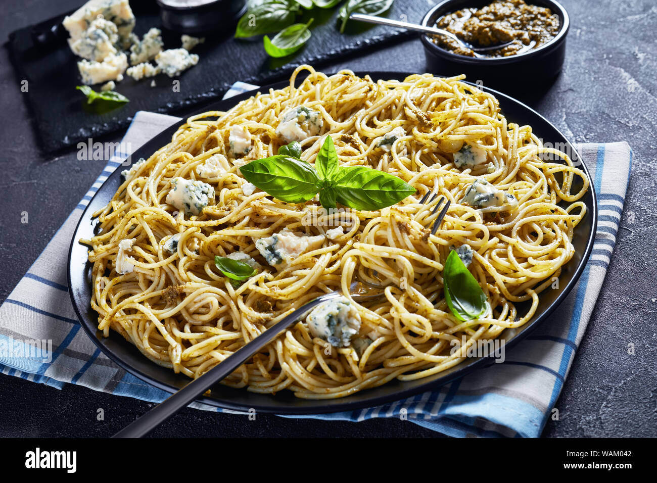 Près de0Spaghetti avec pesto de basilic et de fromage bleu sur une plaque noire sur une table avec le pesto dans un bol noir et ingrédients sur une ardoise cutt Banque D'Images