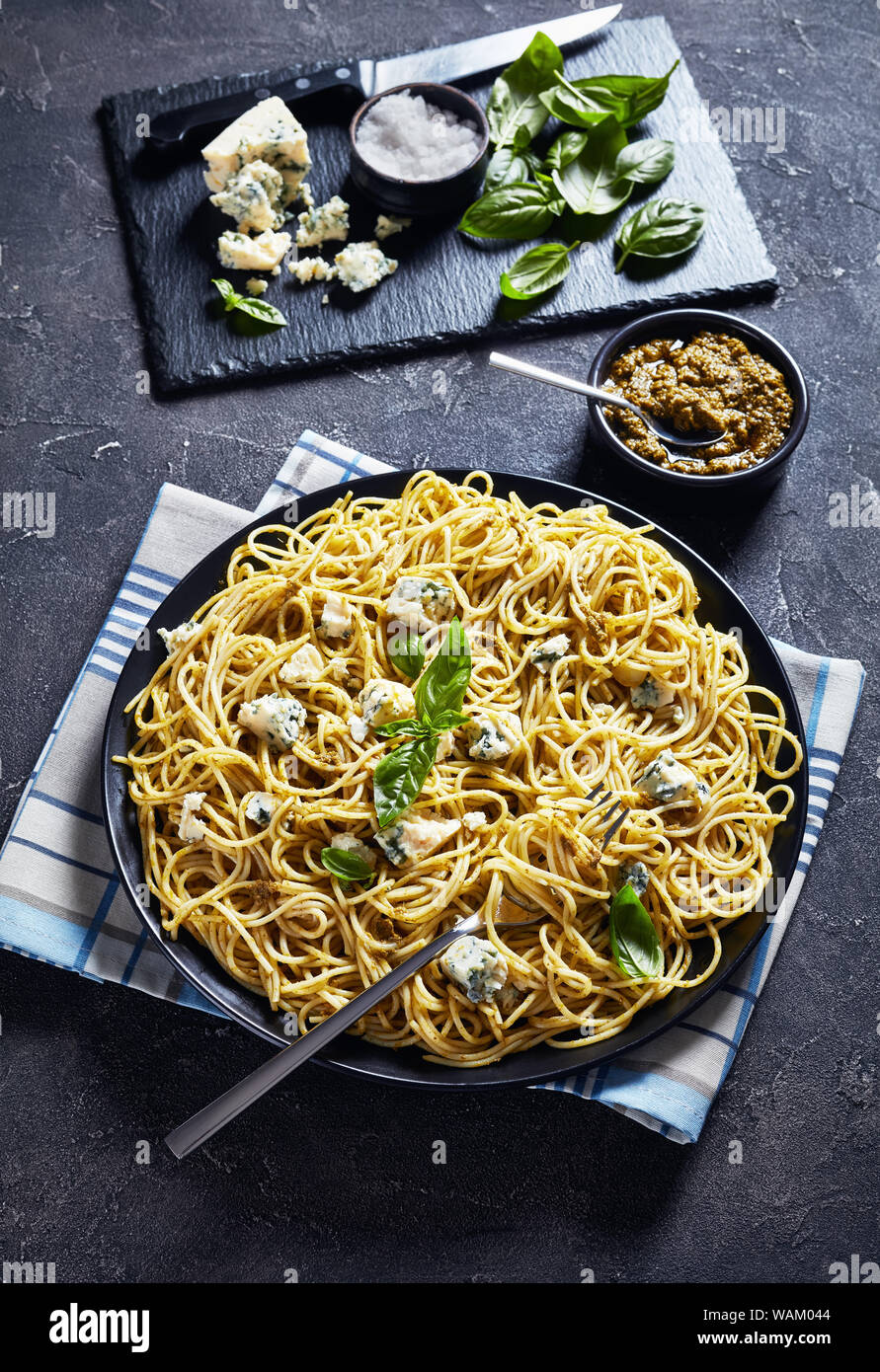 Délicieux spaghetti au pesto de basilic et de fromage bleu sur une plaque noire sur une table avec le pesto dans un bol noir, la cuisine italienne, vue verticale f Banque D'Images