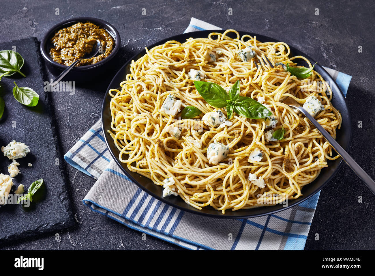 Délicieux spaghetti au pesto de basilic et de fromage bleu sur une plaque noire sur une table en béton, la cuisine italienne, vue horizontale d'en haut Banque D'Images