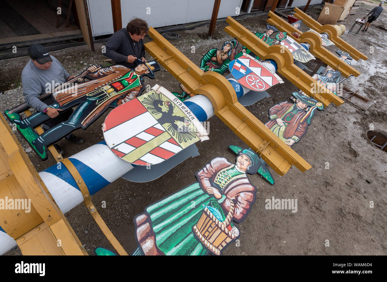 Munich, Allemagne. Août 21, 2019. Costume traditionnel des travailleurs assembler de grandes figures sur une 15 mètres de long, qui est réglé maypole devant une tente à bière sur le site de l'Oktoberfest. Le mât est ensuite abaissé par une grue dans un trou de trois mètres de profondeur (à droite sur la photo). L'Oktoberfest commence cette année le 21 septembre et se termine le 06 octobre. Crédit : Peter Kneffel/dpa/Alamy Live News Banque D'Images