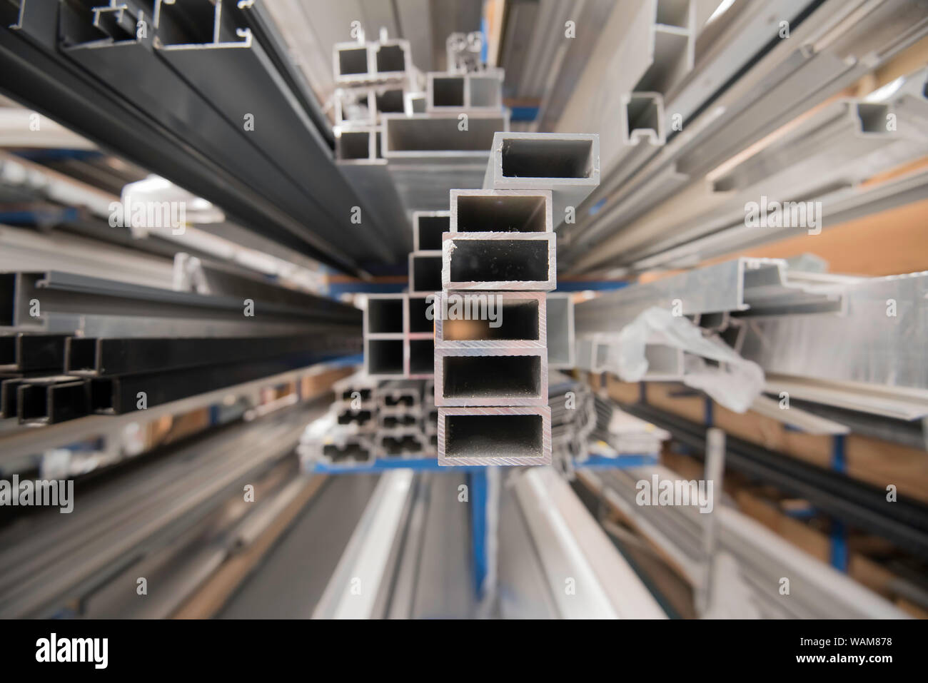Longueurs fraisées de profilés extrudés en alliage d'aluminium (aluminium) assis sur des rayonnages dans un entrepôt et éclairés par la lumière naturelle Banque D'Images