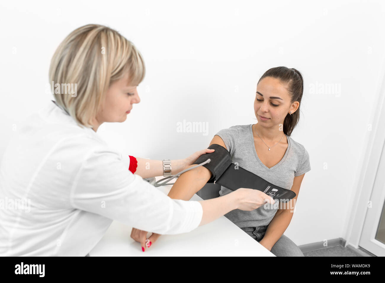 Femme médecin professionnel mise sur l'appareil de mesure de pression sur les jeunes patients de sexe féminin dans la chambre d'hôpital. Banque D'Images