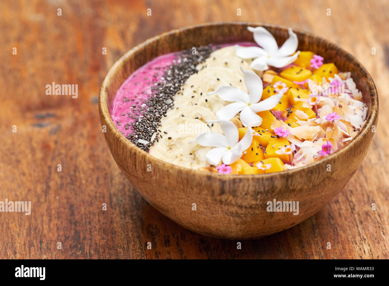Petit-déjeuner Tropical Fruits Bol. La mangue et la banane en bonne santé dans l'alimentation bol en bois sur la table. Végétalien exotique boisson fraîche avec une décoration florale. Mes rêves Banque D'Images