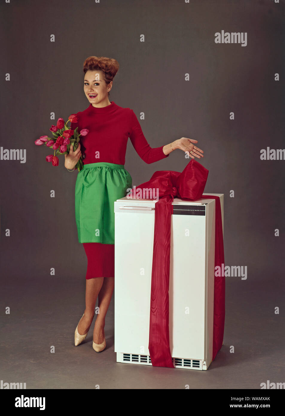 Dans les années 60. Une jeune femme est debout à côté d'un réfrigérateur enveloppé dans un ruban rouge. La Suède des années 1960. ref CV33 Banque D'Images
