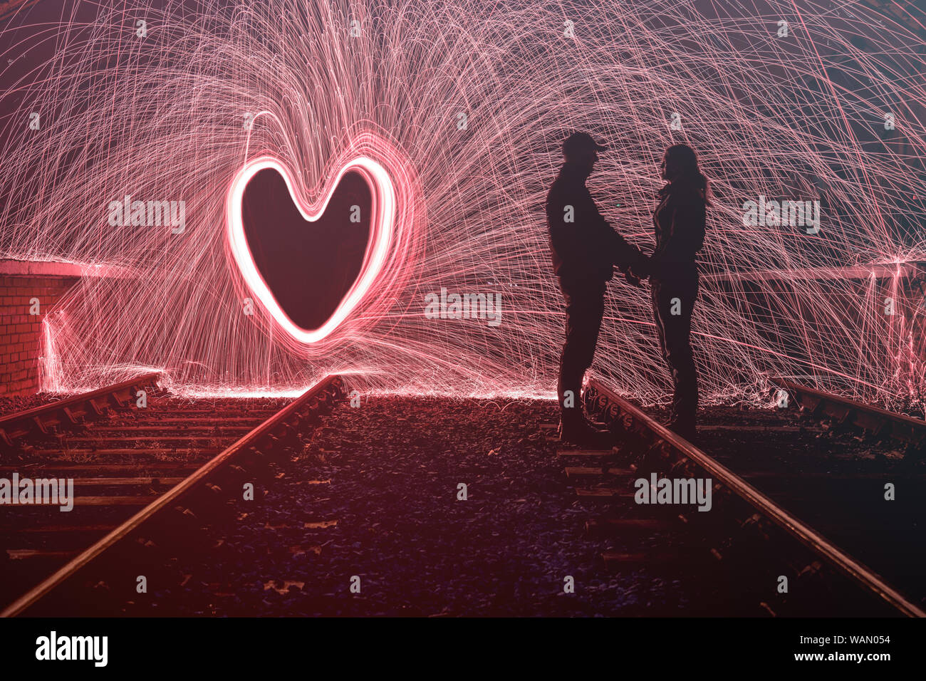 Silhouette de l'homme et de la femme avec des étincelles derrière eux dans une forme de coeur d'amour Banque D'Images
