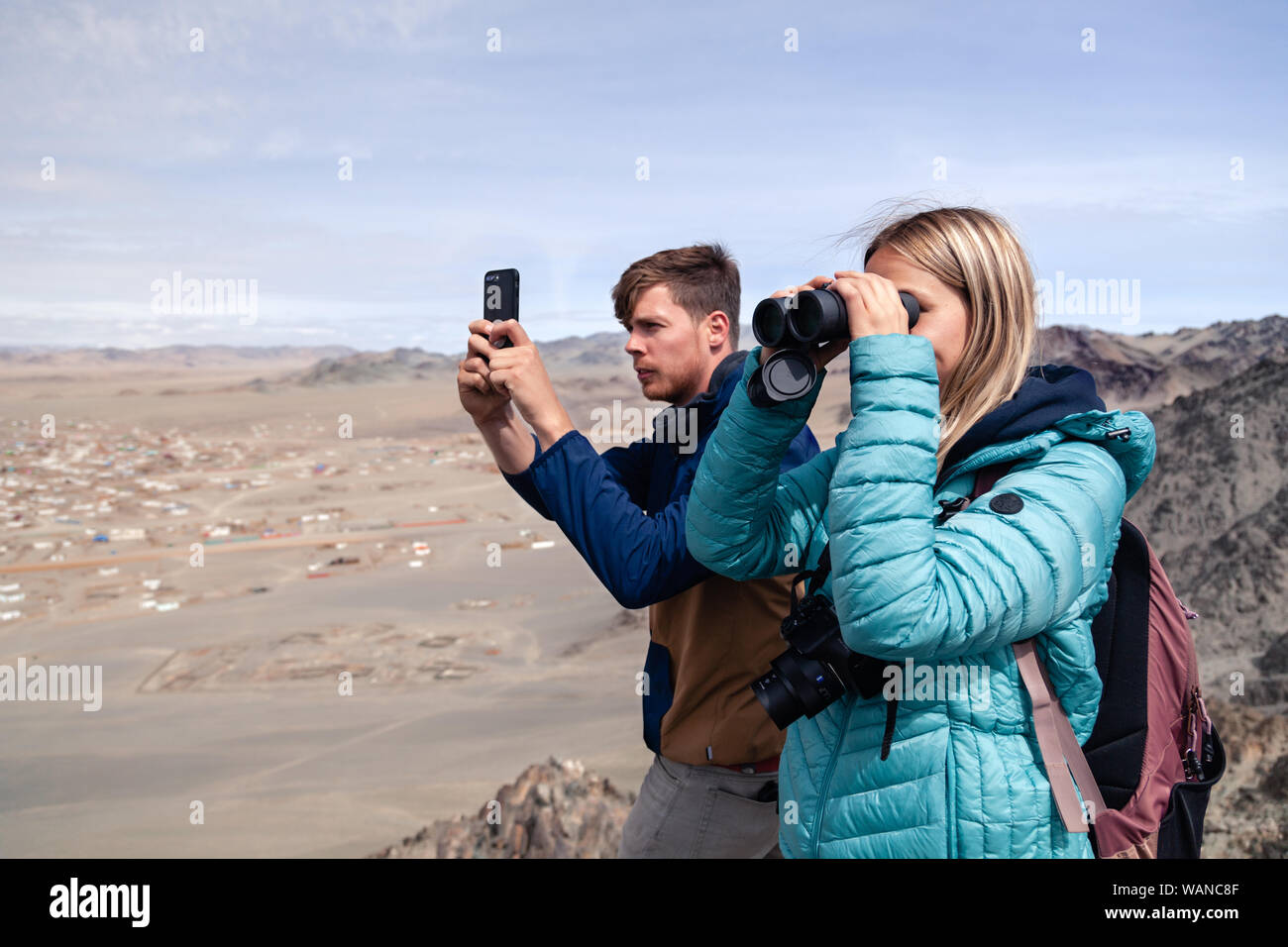 La Mongolie Ulgii 2019-05-04 fille européenne regardant à travers des jumelles et jeune homme faire de photos sur l'appareil photo du smartphone. Sur la montagne à Concept backpackers Banque D'Images