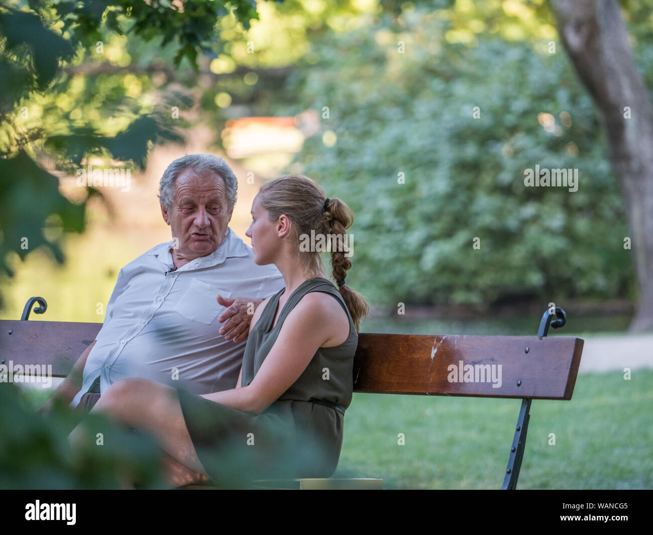 Grand-père et sa petite-fille sont en conversation et passer du temps ensemble. Ils sont assis sur le banc dans le parc. Concept intergénérationnel. Banque D'Images