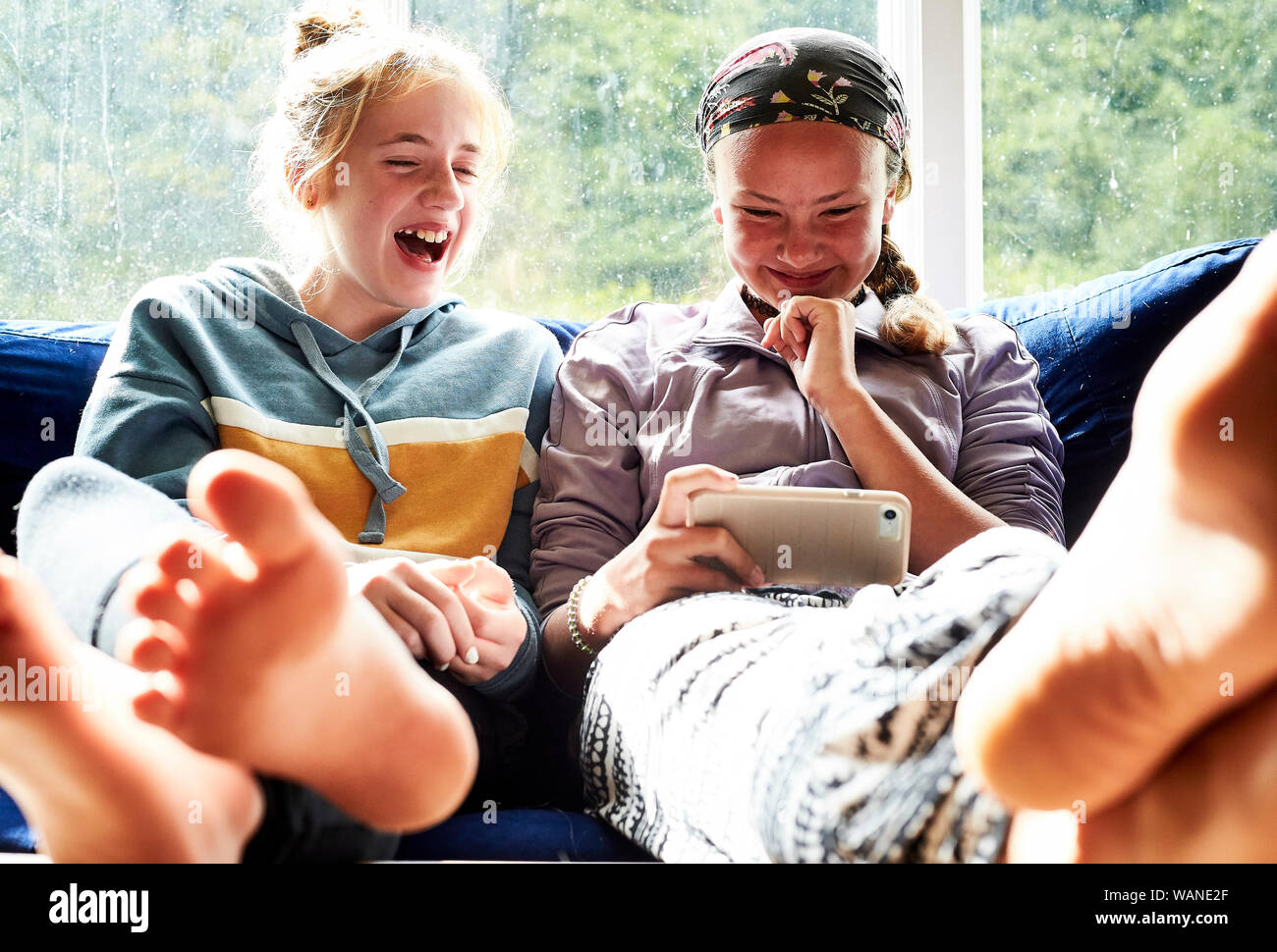 Les jeunes filles assis sur un canapé en regardant un écran et de rire Banque D'Images