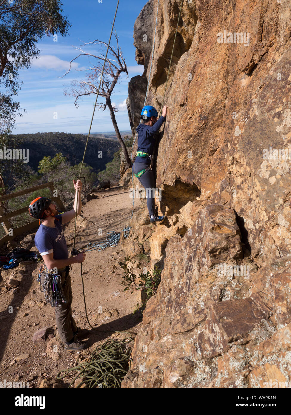 Moniteur d'escalade technique, de l'assurage d'un grimpeur débutant et montrant peur, grimpeur nerveux où placer les mains et les pieds sur la roche face à l'Australie. Banque D'Images